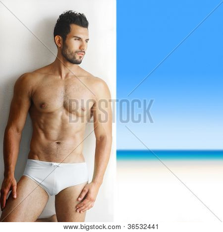 Ritratto sexy di un molto muscoloso torso nudo modello maschile in biancheria intima contro il muro bianco in pos sensuale
