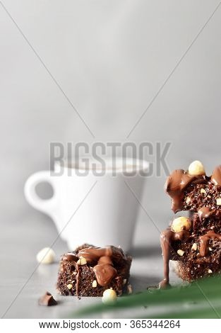 Stack Of A Brownie Pieces With Hazelnut, Palm And Cup On A Grey Table With Gray Background.