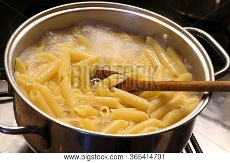 Pot With Boiling Water And The Italian Pasta During Cooking And A Wooden Spoon To Mix