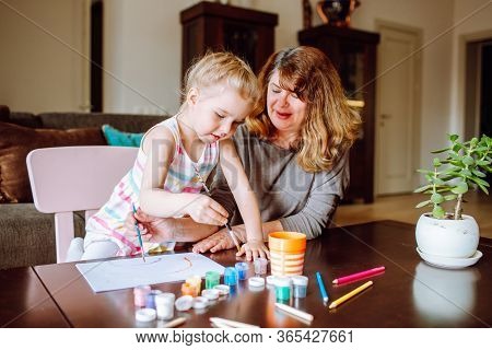 Grandmother And Granddaughter Drawing Together With Watercolors At Home. Little Girl With Her Drawin