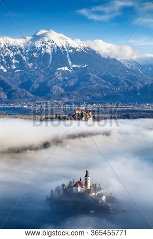 amazing panorama of Lake Bled Blejsko Jezero on a foggy morning with the Pilgrimage Church of the Assumption of Maria on a small island and Bled Castle and Julian Alps in backgroud