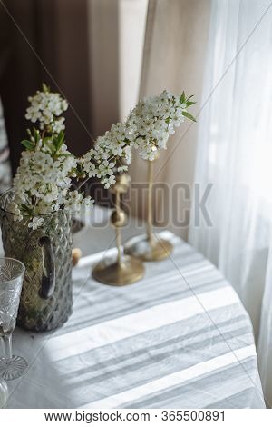 Flowering Branch With White Flowers In A Vase On A White Table A Glass And Gold Candlesticks