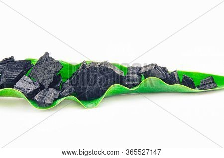 Natural black wood cosmetic activated charcoal or mineral with medicinal properties on green leaf isolated on white background.