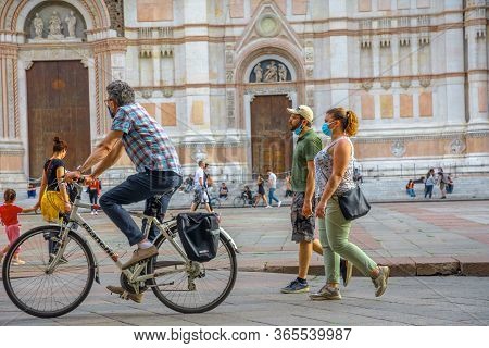 Bologna, Italy - May 9, 2020: Man Riding Bike With Surgical Mask In Piazza Maggiore Central Square W