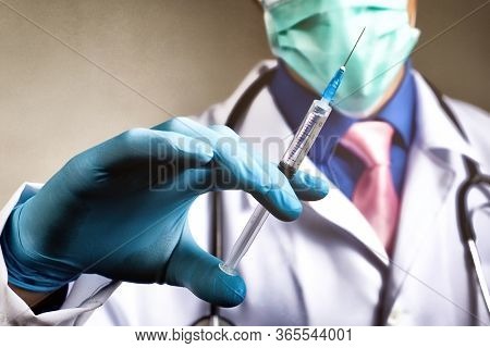 Doctor In Gauze Mask And Medical Robe Holding Syringe In His Blue Rubber Glove Dressed Hand. Health 