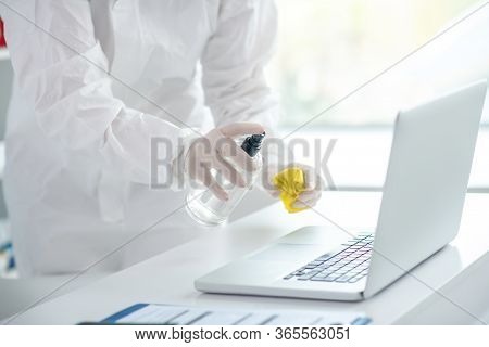 Person In Protective Workwear Sparying Sanitizer On The Laptop