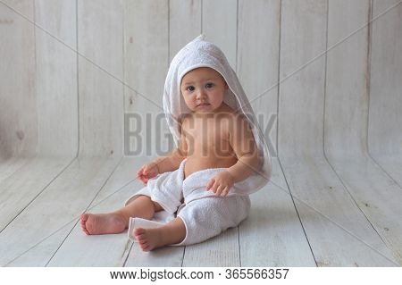 One Yeat Old Baby Girl Is Sitting On Wooden Backgroun In White Towel. After Bath Time.