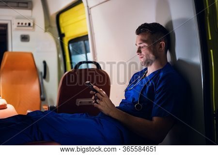 Young Paramedic Sitting With His Smartphone In The Ambulance Car
