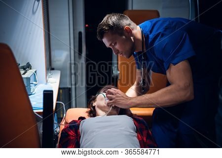Young Corpsman Applies An Oxygen Mask To An Injured Woman Lying On A Stretcher In An Ambulance Car