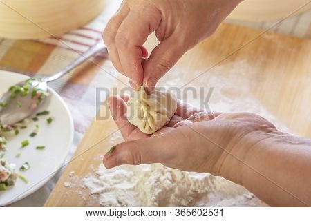 Female Hands Are Preparing Manti, Dumplings Or Wonton From Dough With Meat Filling On The Background