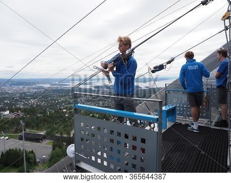 Oslo, Norway On July 2019: Three Men Care About Zipline Rider In European City Seen From Ski Jump In