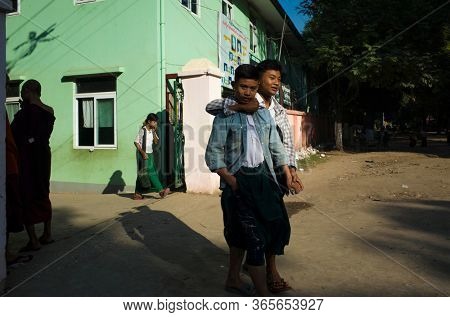 Amarapura, Mandalay, Myanmar - January 14, 2020: Children go out from school gate. Two teenage boys hanging around and playful hugging
