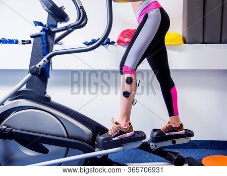 Young Sports Woman With Electrostimulator On The Muscles Of The Legs.