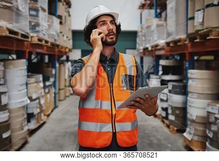 Tensed Warehouse Manager Holding Digital Tablet While Talking On Mobile Phone Looking Stressed