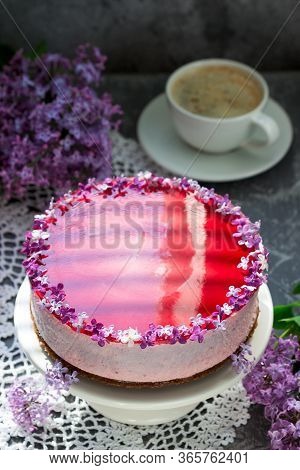 A Berry Mousse Cake With Chocolate Base And Juice Jelly, Decorated With Lilac Flowers, Served With C