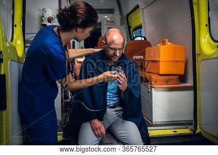 Young Nurse Giving An Oxygen Mask To A Man Sitting In An Ambulance