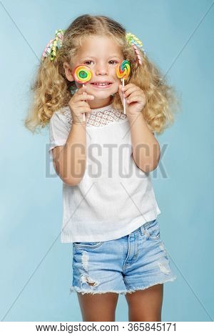 A Child With A Candy. Little Girl With A Round Candy In The Studio On A Blue Background.