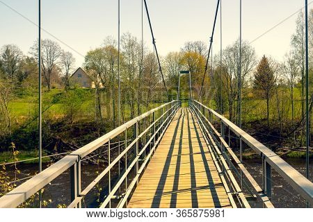 Suspension Bridge Over The Salaca River In Latvia In The National Park In Spring On A Sunny Day