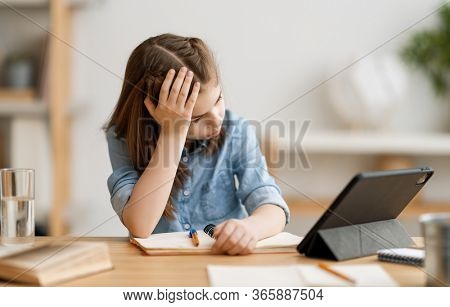 Back to school. Unhappy child is sitting at desk. Girl doing homework or online education.
