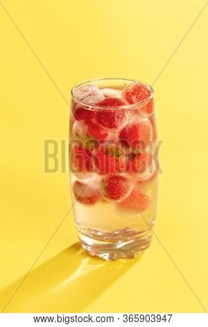 Glass Of Water With Frozen Strawberries On A Yellow Background. Coldwater With Iced Fruits