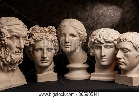Group Gypsum Busts Of Ancient Statues Human Heads For Artists On A Dark Background. Plaster Sculptur