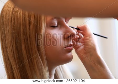 Close-up Of Makeup Artist Painting Arrows On Clients Face. Macro Shot Of Young Blonde Woman Visiting