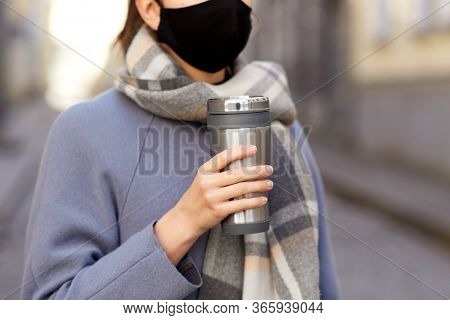 health, safety and pandemic concept - young woman wearing black face protective reusable barrier mask with tumbler or thermo cup on city street