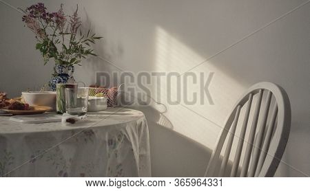 Table With A Tablecloth, Flowers And Fruits. White Chair. Sunlight.