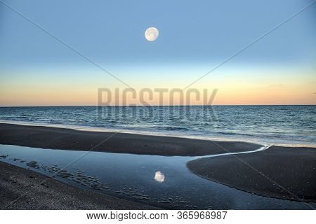 Reflection Of The Full Moonset In A Tidal Pool In Front Of The Ocean On Naples Beach In Naples, Flor
