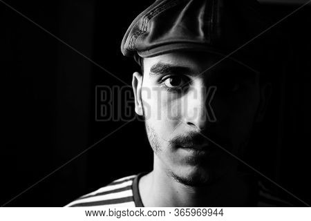 Black And White Portrait Of Cute Young Guy With Moustache And A Hat On Black, Dark Background.
