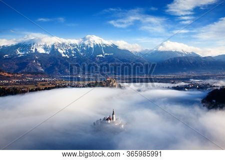 amazing panorama of Lake Bled Blejsko Jezero on a foggy morning with the Pilgrimage Church of the Assumption of Maria on a small island and Bled Castle and Julian Alps in backgroud