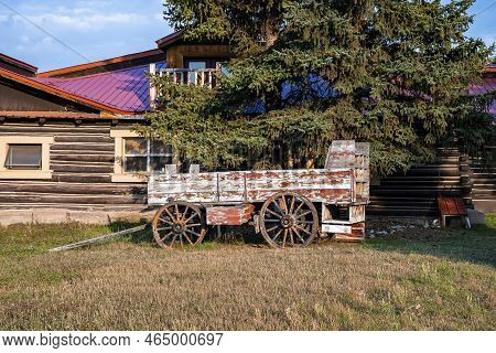 Old Obsolete Wagon Under Tree Against Log Cabin During Sunny Day