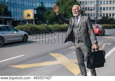Smiling Entrepreneur Hailing For Cab While Carrying Laptop Bag. Successful Senior Businessman Is Wav