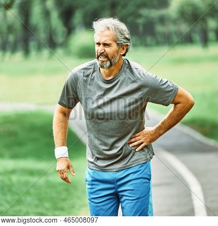 Portrait Of A Senior Man Exercising And Running Outdoors Having Chest Or Stomack Or Hip Or Back Pain