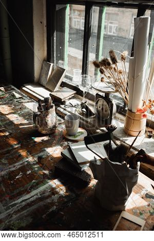 Stucco Vase And Jug With Art Tools Near Books And Vintage Scales On Rough Windowsill With Paint Spot