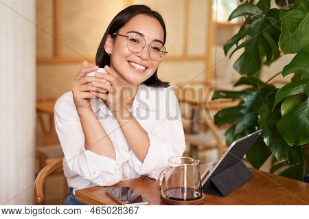 Smiling Asian Girl In Glasses, Woman Working On Remote, Drinking Coffee And Using Tablet