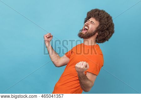 Side View Of Excited Positive Happy Man With Afro Hairstyle Wearing Orange T-shirt Screaming For Joy