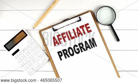 Affiliate Program Words On A Clipboard, With Calculator, Magnifier And Pencil On The White Wooden Ba