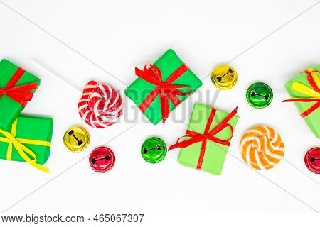 Happy Holidays: Gifts With Lollipops And Red, Green, Golden Bells On A White Background, Copy Space.