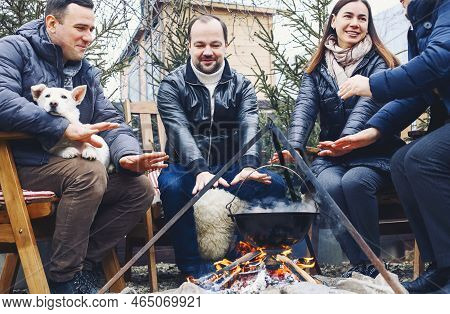 Traditional Mulled Wine With Slices Of Orange Preparing In Pot Over Burning Logs In Winter In Countr