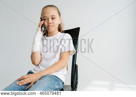 Portrait Of Cute Blonde Little Girl With Broken Arm Wrapped In Plaster Bandage Talking Smartphone, S