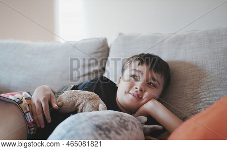 Indoor Portrait Kid Looking Up With Smiling Face, Happy Boy Lying On Sofa Watchig Tv Or Relaxing In 