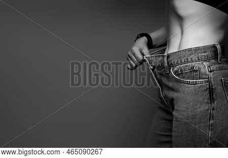 Attractive, Slender Young Woman In Her Thirties, Dressed In Wide Jeans And A White Shirt, Demonstrat