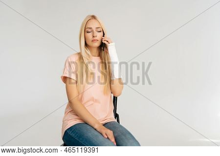 Portrait Of Sad Depressed Young Woman With Broken Arm Wrapped In Plaster Bandage Talking Mobile Phon