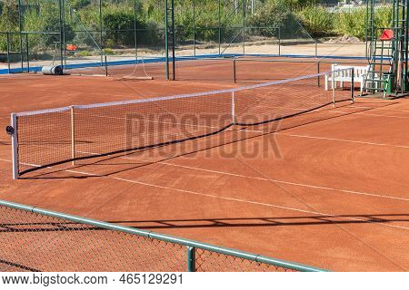 Baseline And Net Of An Empty Clay Tennis Court On A Sunny Day
