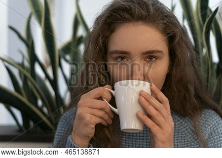 Portrait Of Young Girl With Thick Brown Hair With Cup Of Tea On Green Plants Background. Girl With N