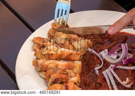A Man Eats Beef Goulash With Czech Dumplings With A Knife And Fork.