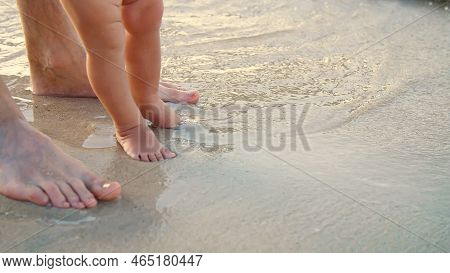 Close-up, On Wet Sand, There Are Male And Childrens Feet. A Wave Comes In. Vacation On Ocean Beach, 