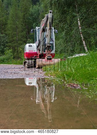Umhausen, Austria - July 26, 2022: A Working Machine - A Digger - And Its Reflection In A Rain Puddl