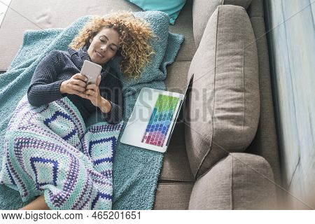 Reaxed Caucasian Woman Type And Use Mobile Phone Device Lay Down On The Sofa Covered With Blue Blank